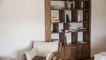 Een kamer met een houten boekenkast, een beige fauteuil en een klein rond voetenbankje.