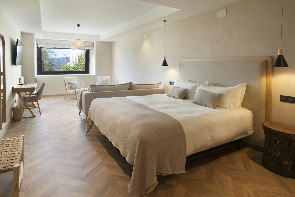 A modern bedroom with a large bed, a sofa, a dining table, and a TV.