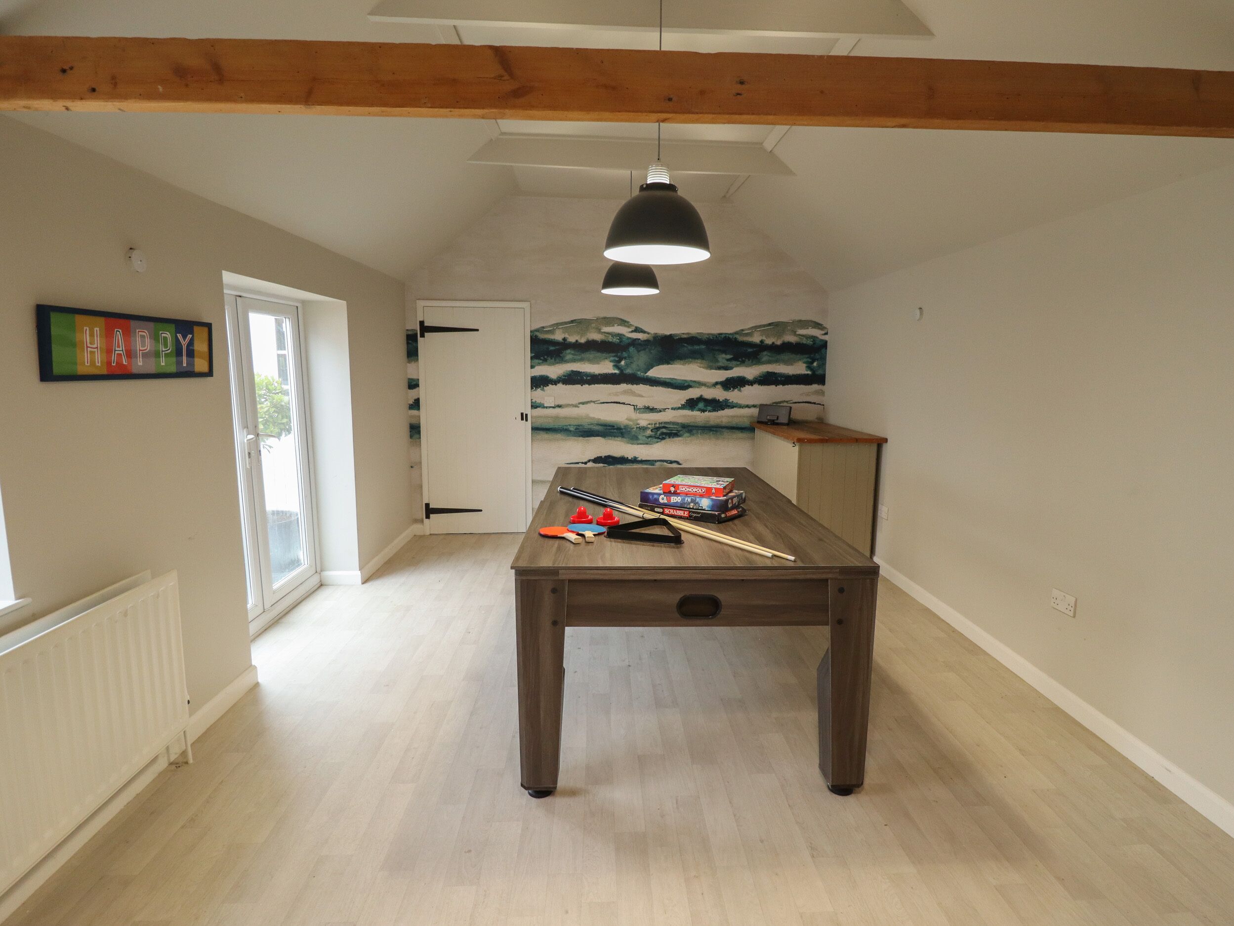 A room with a wooden table, a pool table, a door, a radiator, and a wall with a 'HAPPY' sign.