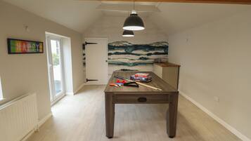 A room with a wooden table, a pool table, a door, a radiator, and a wall with a 'HAPPY' sign.