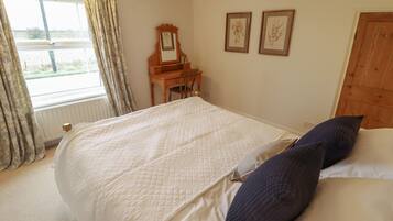 Un dormitorio con una cama, un aparador de madera, un ventanal con cortinas y dos impresiones enmarcadas de motivos botánicos en la pared.