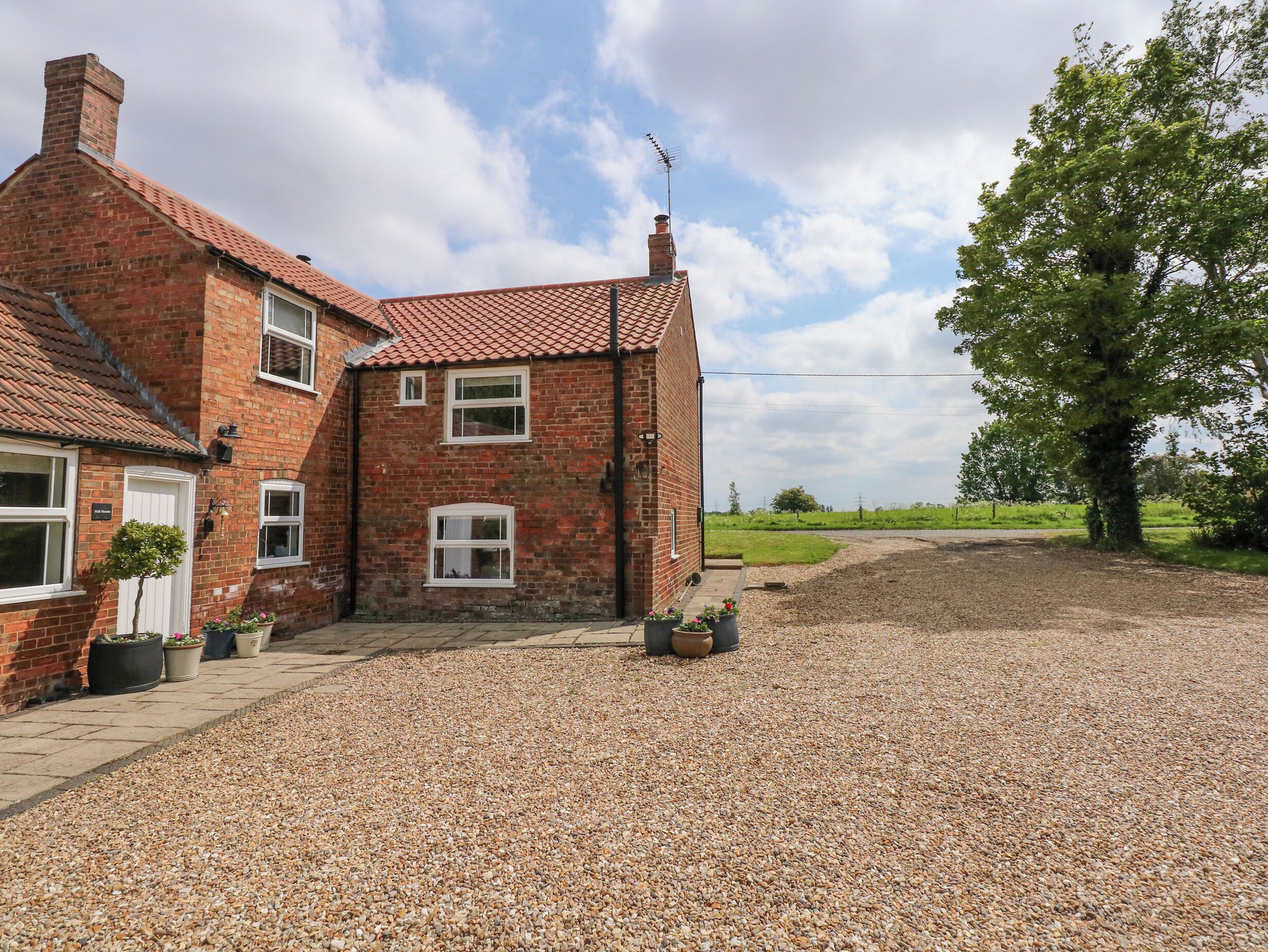 A two-story brick house with a gravel driveway and a small garden area.