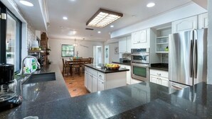 Una cocina moderna con encimeras de granito, electrodomésticos de acero inoxidable y una zona de comedor con mesa y sillas de madera.
