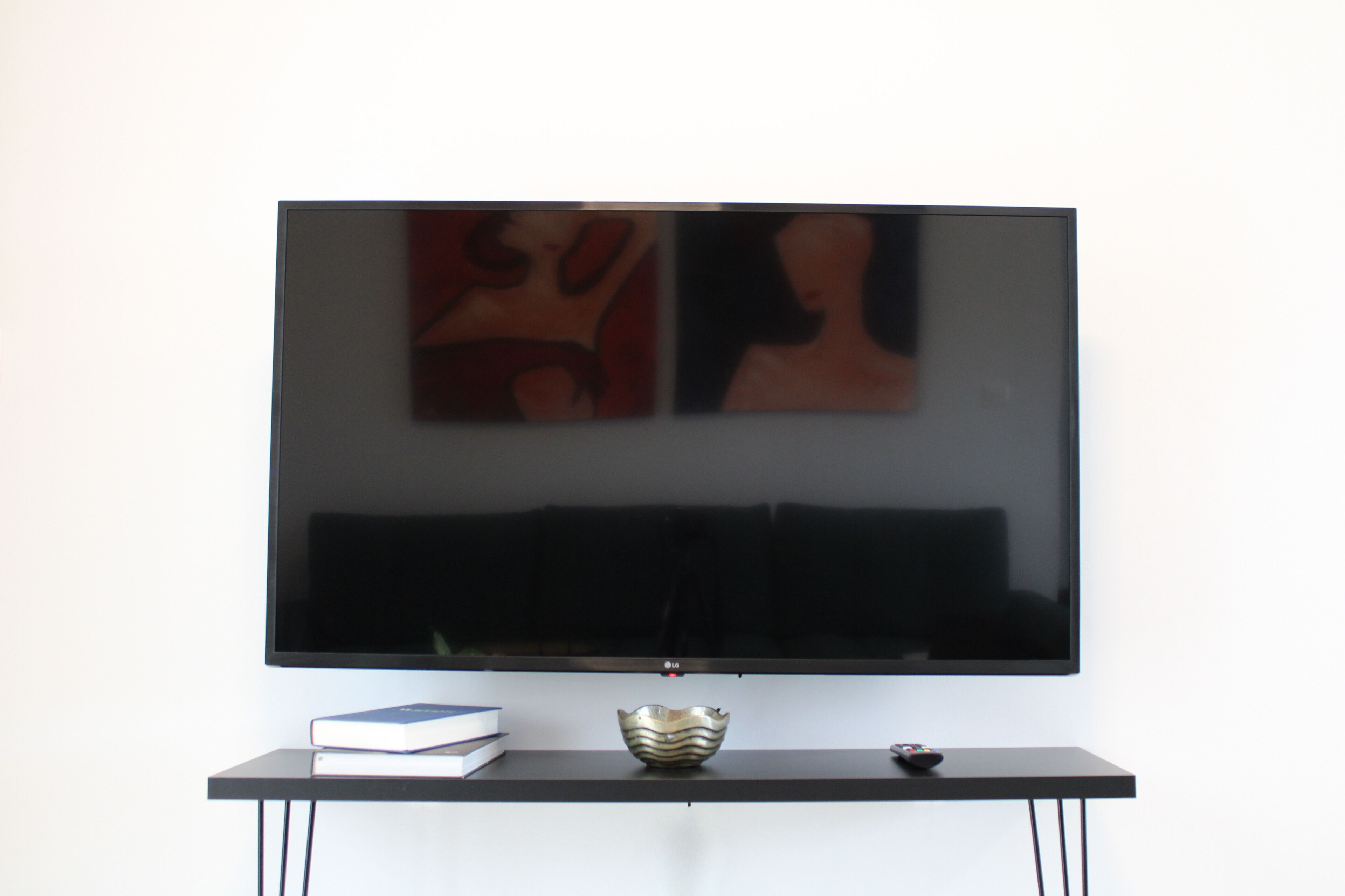 Un televisore a schermo piatto montato a parete sopra un tavolo consolle nero con una ciotola decorativa e un telecomando.