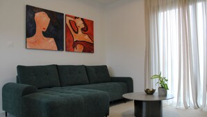 A modern living room with a dark green sectional sofa, a round coffee table, and two abstract paintings on the wall. - Hypnos Residence (Ayios Dhometios)