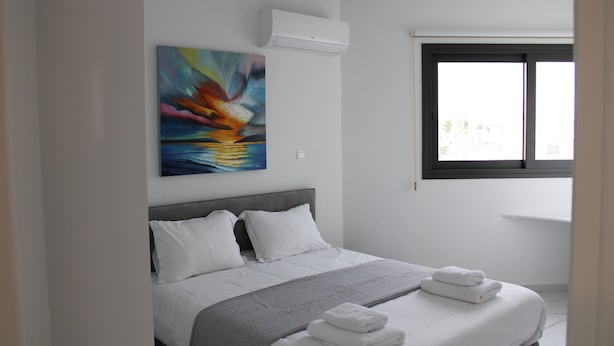 A modern hotel room with a neatly made bed, a painting on the wall, and a window with a view. - Hypnos Residence (Ayios Dhometios)