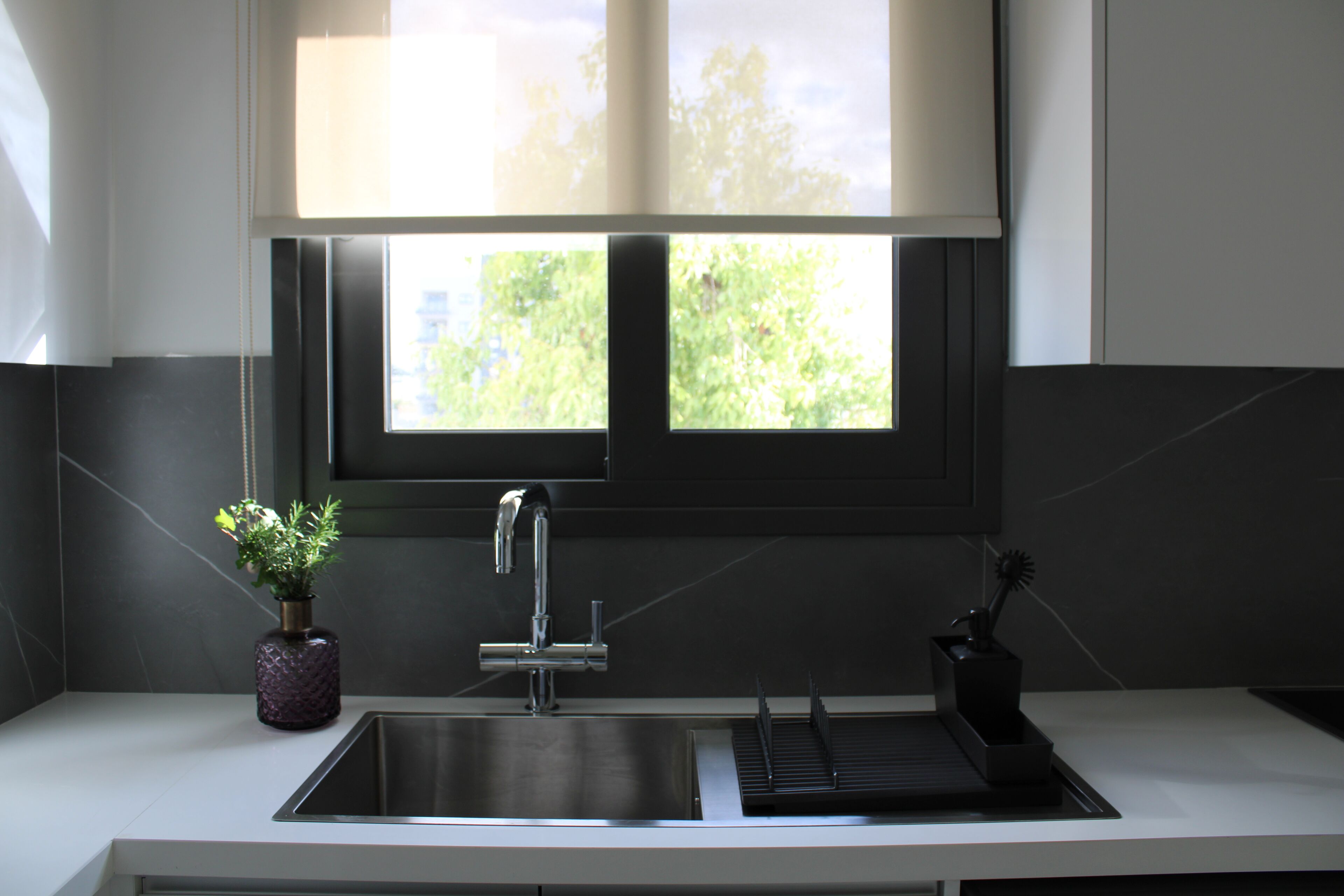 Cocina moderna con un lavamanos de acero inoxidable, una planta en maceta y una ventana con vistas a zonas verdes.