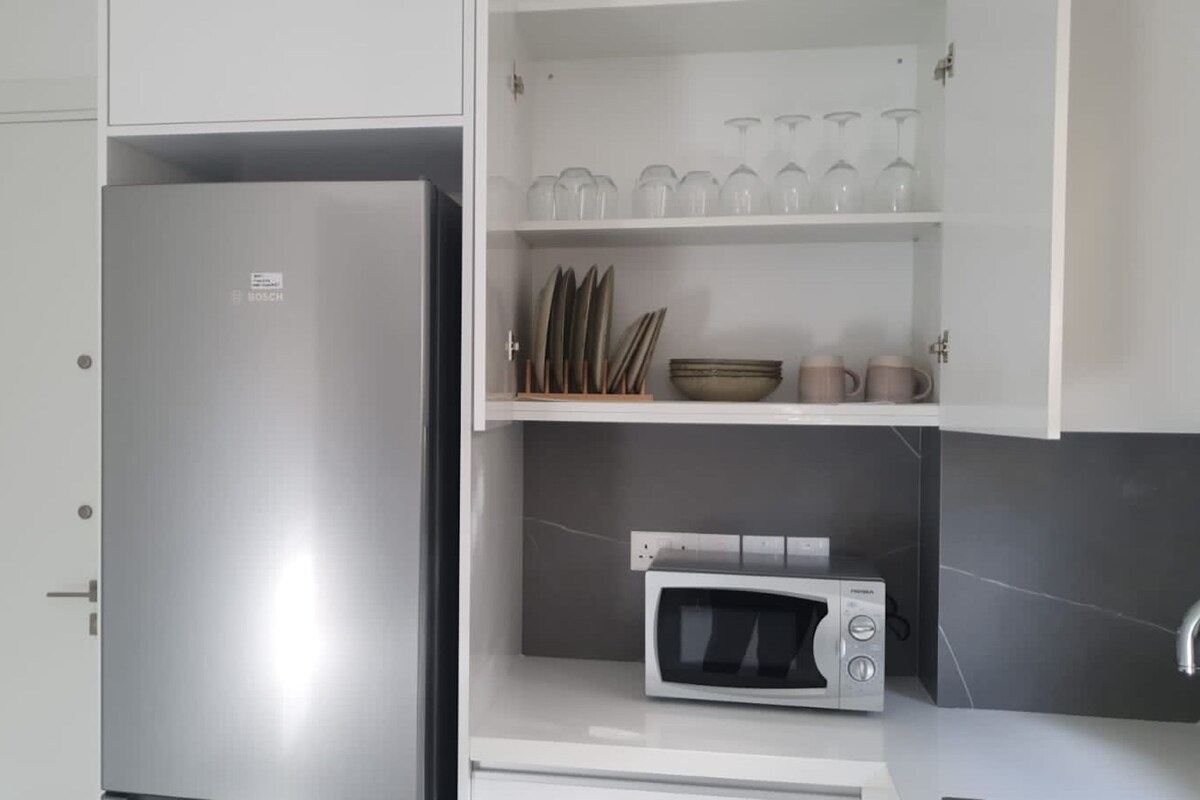A kitchen with a stainless steel refrigerator, a microwave, and shelves with glassware and kitchen utensils.