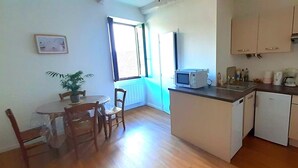 Cocina compacta con microondas, pileta y alacenas. Cuenta con una zona de comedor con mesa y sillas, y una planta en maceta.