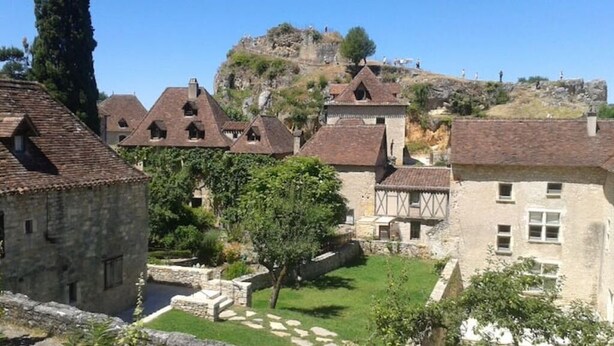 Un pueblo histórico con edificios de piedra, un patio central y una colina al fondo.