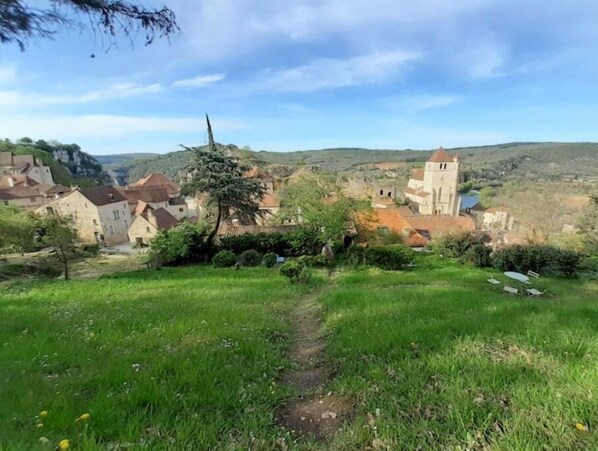 Un pueblo rural con edificios de piedra, una iglesia y un sendero que serpentea entre la vegetación.