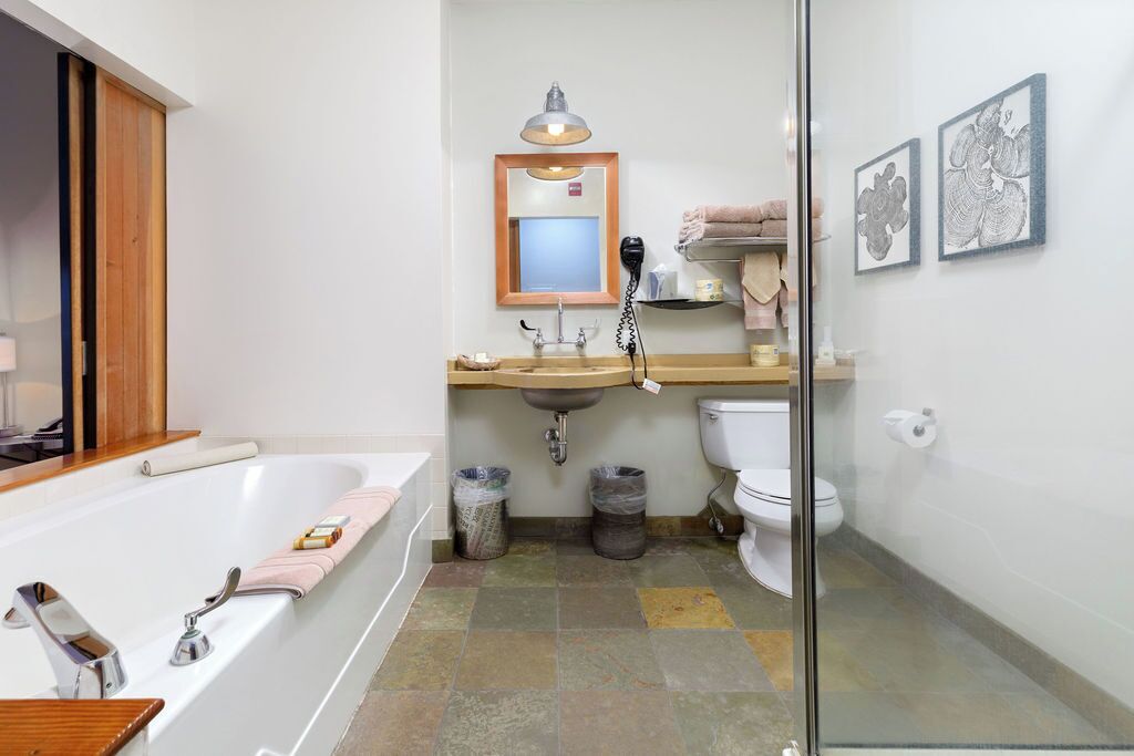 Un baño moderno con bañera, lavabo e inodoro. Hay un espejo sobre el lavabo, un secador de pelo en la encimera y dos cestos de basura.