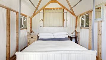 Habitación individual con cama, techo de madera, paredes blancas y ventana a un lado.