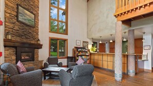 Ein großzügiges Wohnzimmer mit Kamin aus Stein, bequemen Sitzmöglichkeiten, einem Couchtisch und einer Bar mit Blick ins Freie.