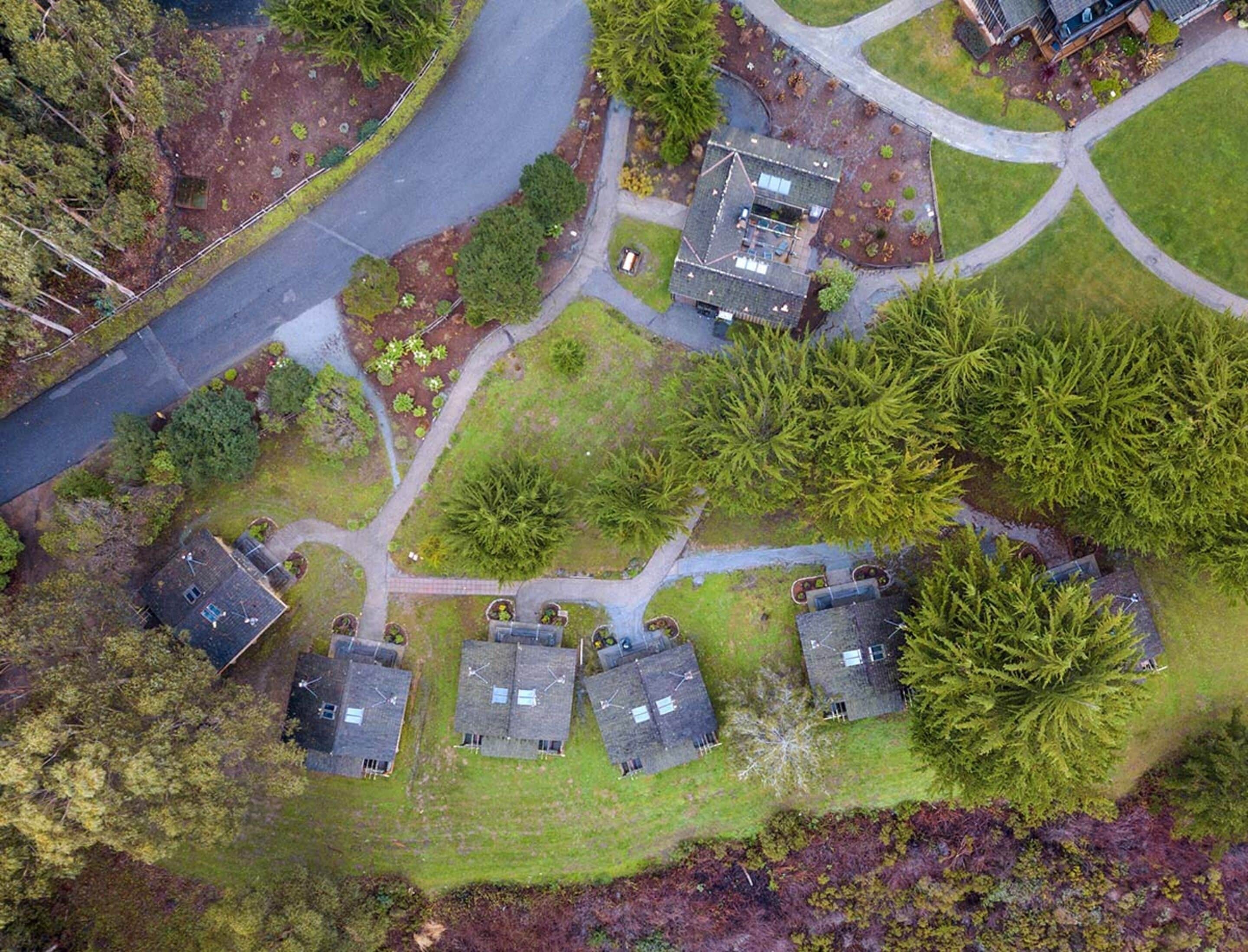 An aerial view of a residential area with multiple houses, green lawns, and a winding road.