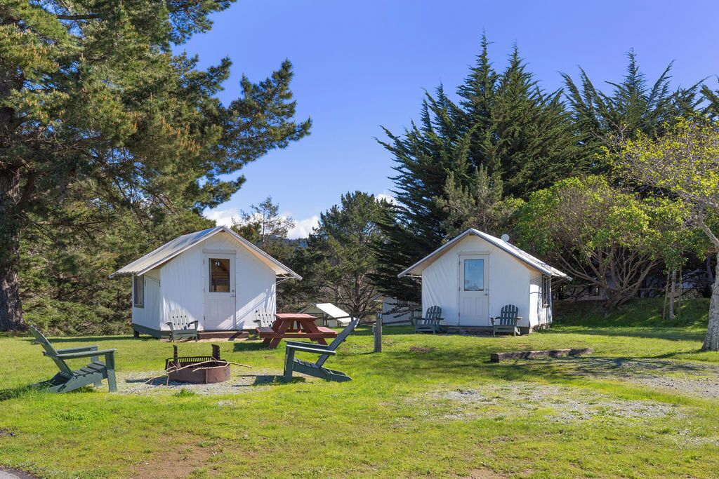 Two small cabins with a picnic table and chairs in a grassy area surrounded by trees.