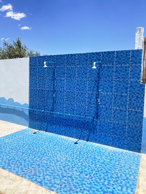 A blue-tiled outdoor shower area with a white wall and a blue-tiled floor. - IGHIZ INN Resort (Errachidia)