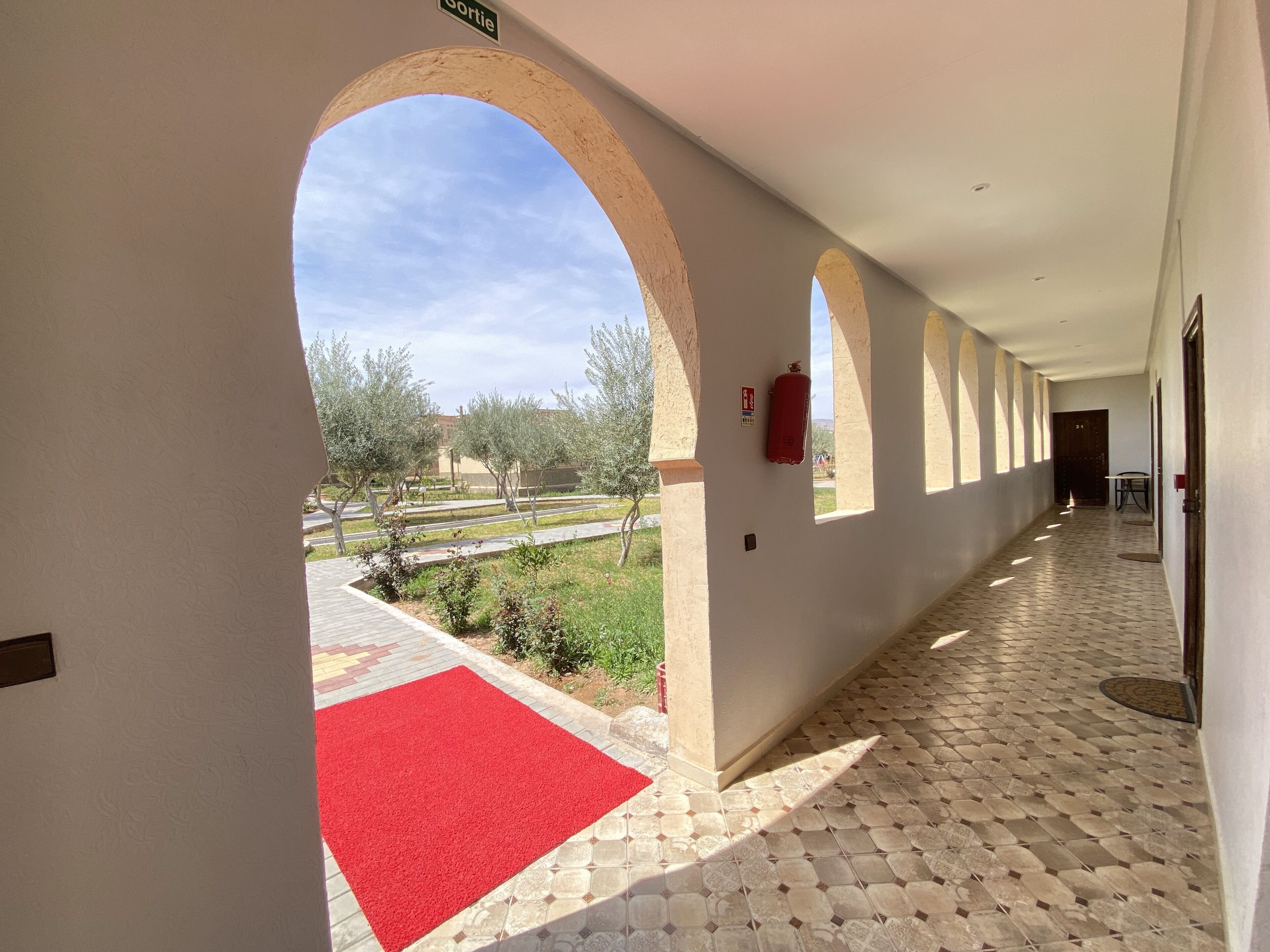 A corridor with arches, a red carpet, and a fire extinguisher.