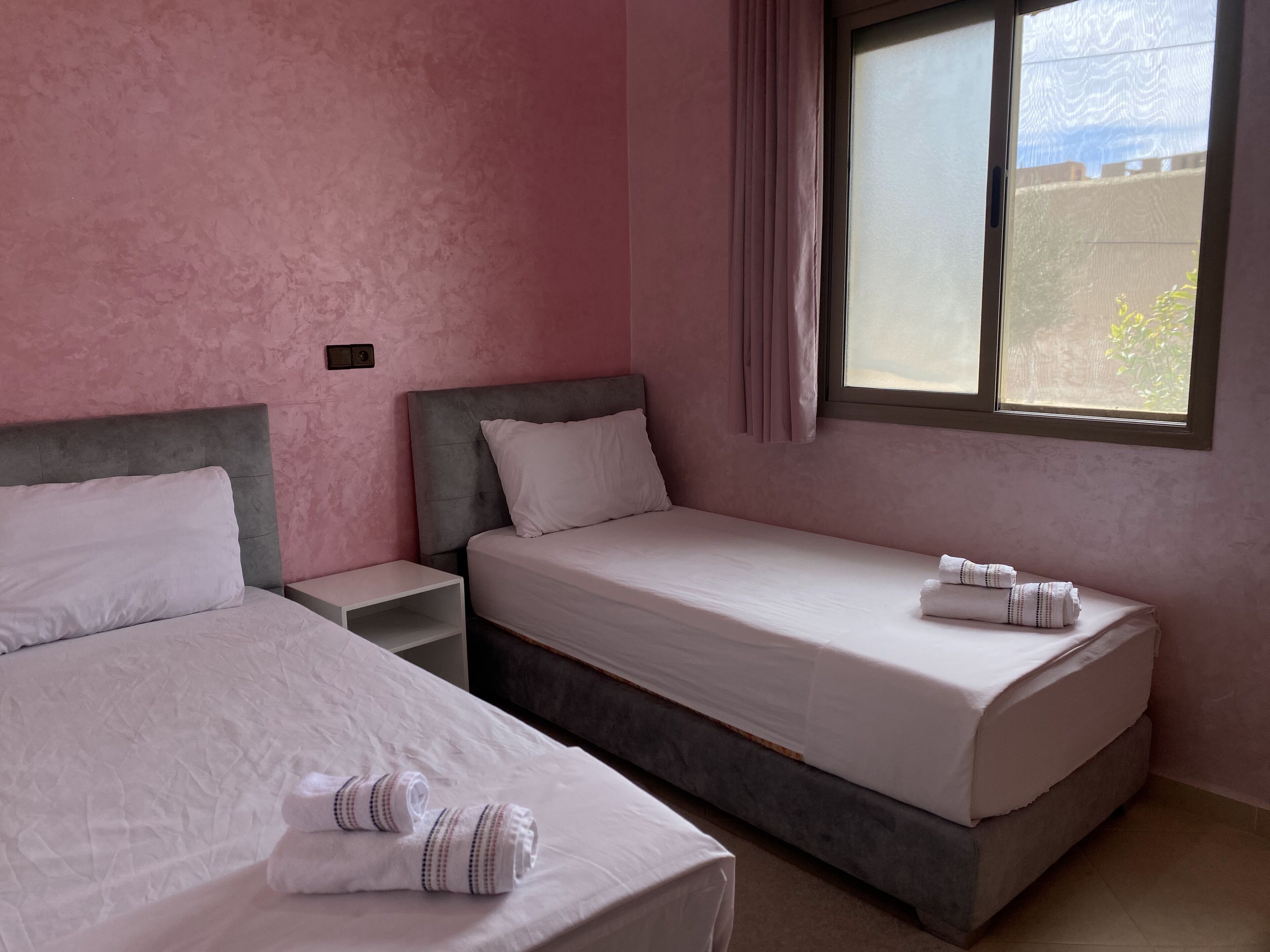 A room with two beds, a nightstand, and a window with curtains.
