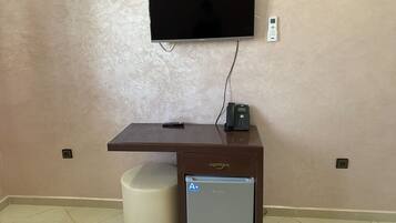 A small, dark wooden desk with a mounted flat-screen TV, a telephone, and a small refrigerator.