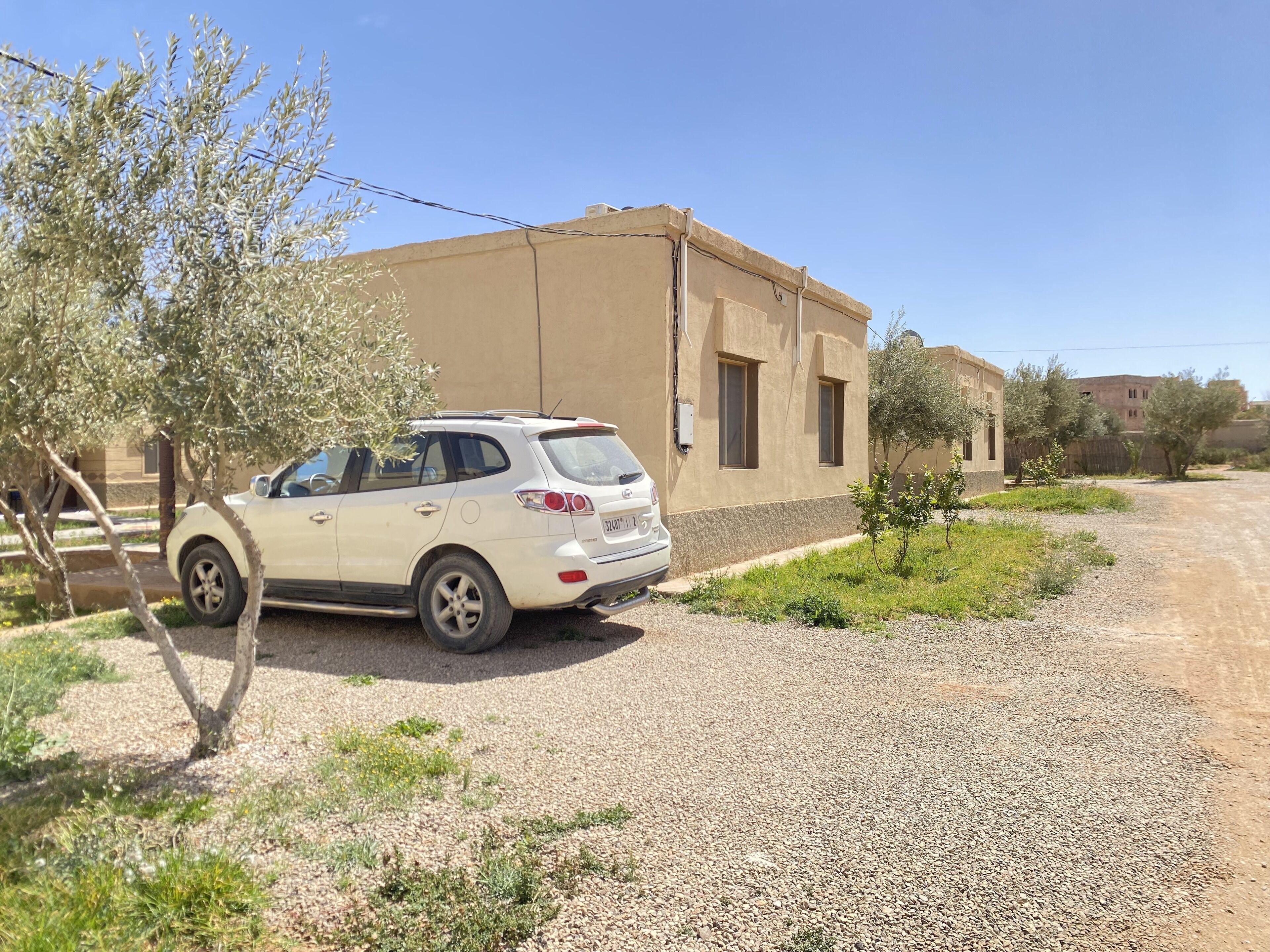 A white SUV parked on a gravel driveway in front of a beige building with two windows and a door.