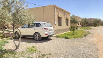 A white SUV parked on a gravel driveway in front of a beige building with two windows and a door.