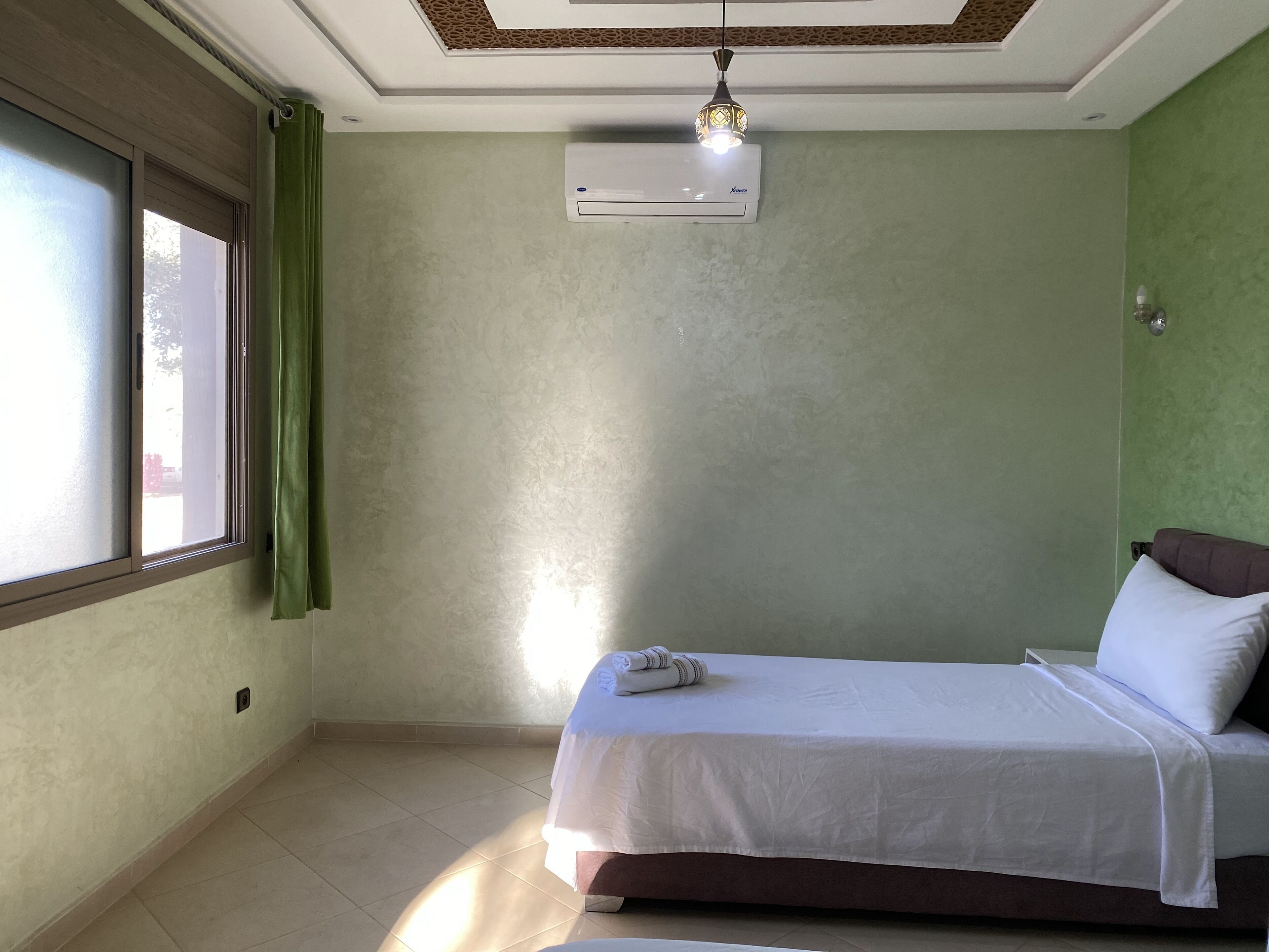 Un dormitorio con cama, aire acondicionado, ventana con cortinas e iluminación en el techo.