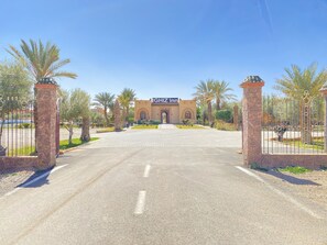 A gated entrance to a hotel with a clear sky, palm trees, and a sign reading "IGHZ Inn". - IGHIZ INN Resort (Errachidia)