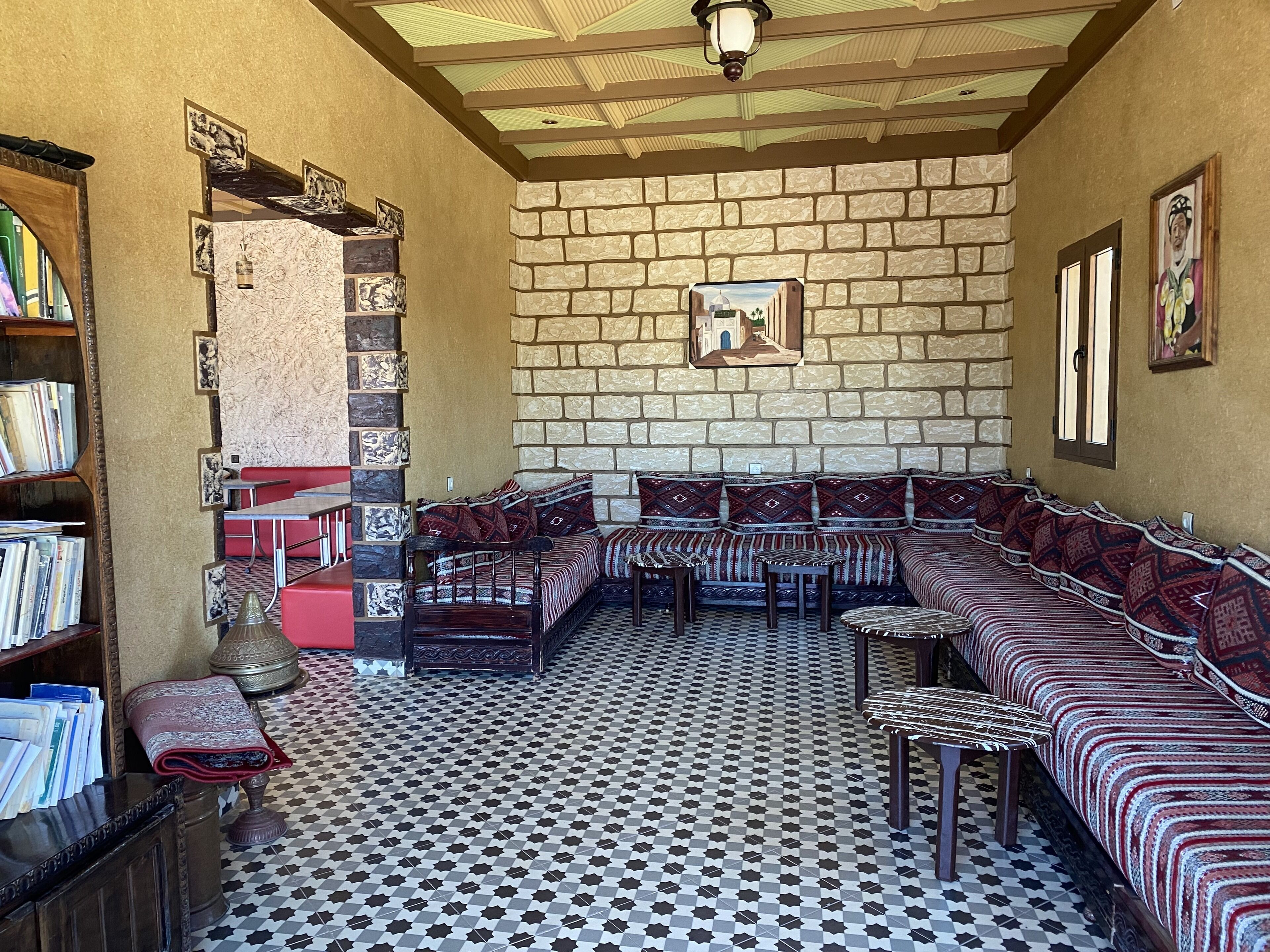 A library with bookshelves, a reading area with sofas and tables, and a patterned floor.