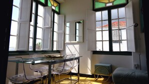 A room with a glass table, clear plastic chairs, a small round table, and a green cushioned bench.