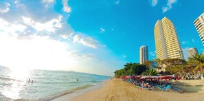 Ein Strand mit einer Reihe hoher Gebäude, Sonnenschirmen und Menschen.