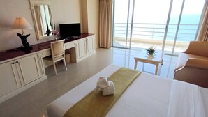 Une chambre d’hôtel avec un lit, un bureau avec une télévision, une chaise, une petite table et une vue sur l’océan.