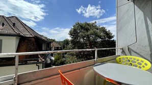 Ein Balkon mit Tisch und Stühlen, einem Geländer und Blick auf ein Gebäude und Bäume.