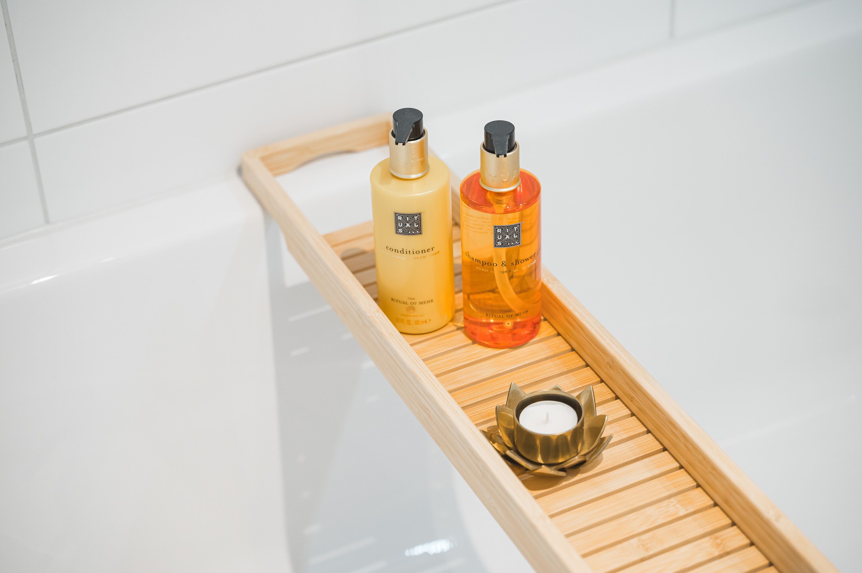 Uma bandeja de madeira com duas garrafas de condicionador e shampoo, e uma vela em uma banheira.