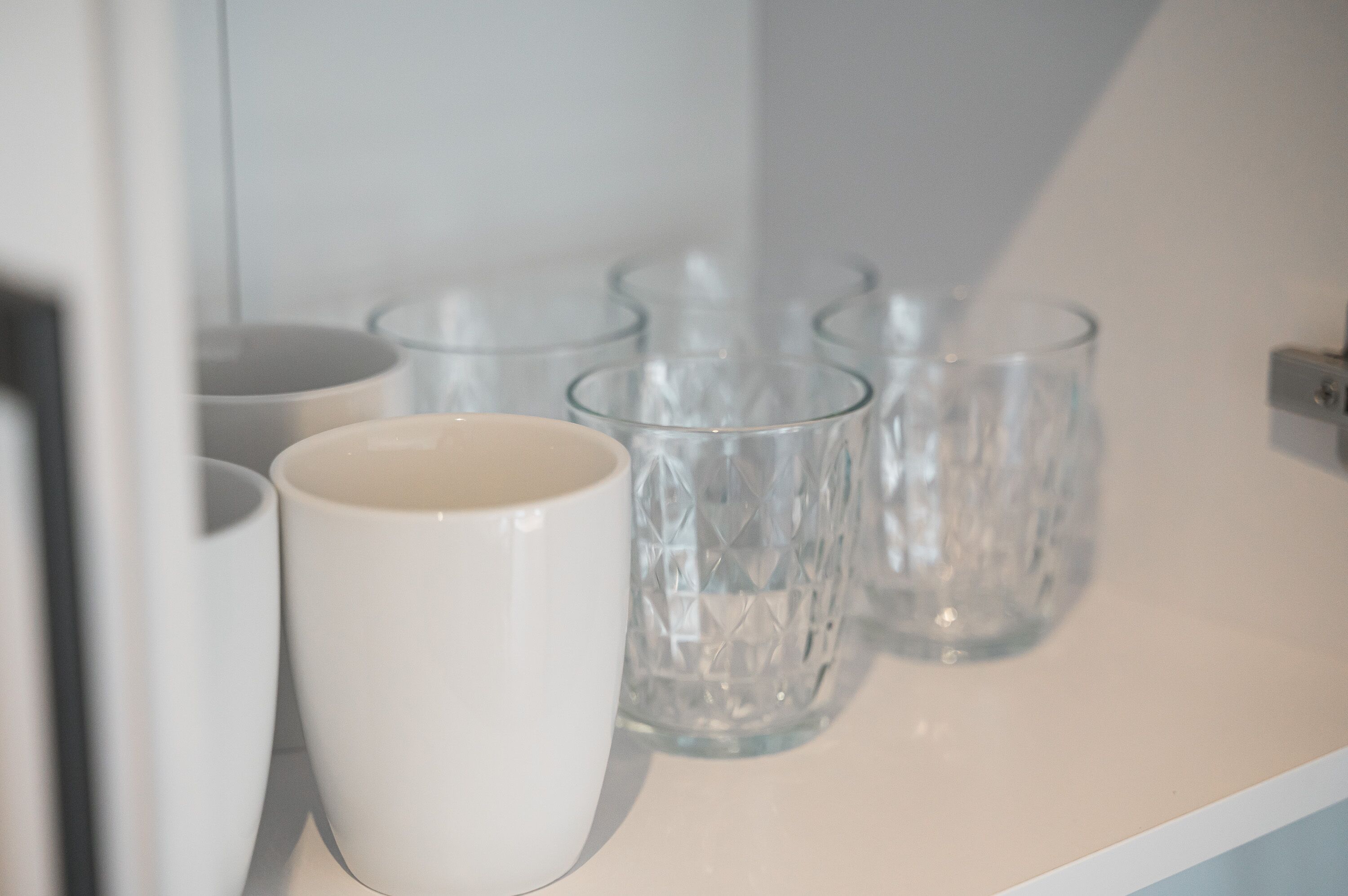 Une étagère blanche avec de la verrerie transparente et une tasse blanche.