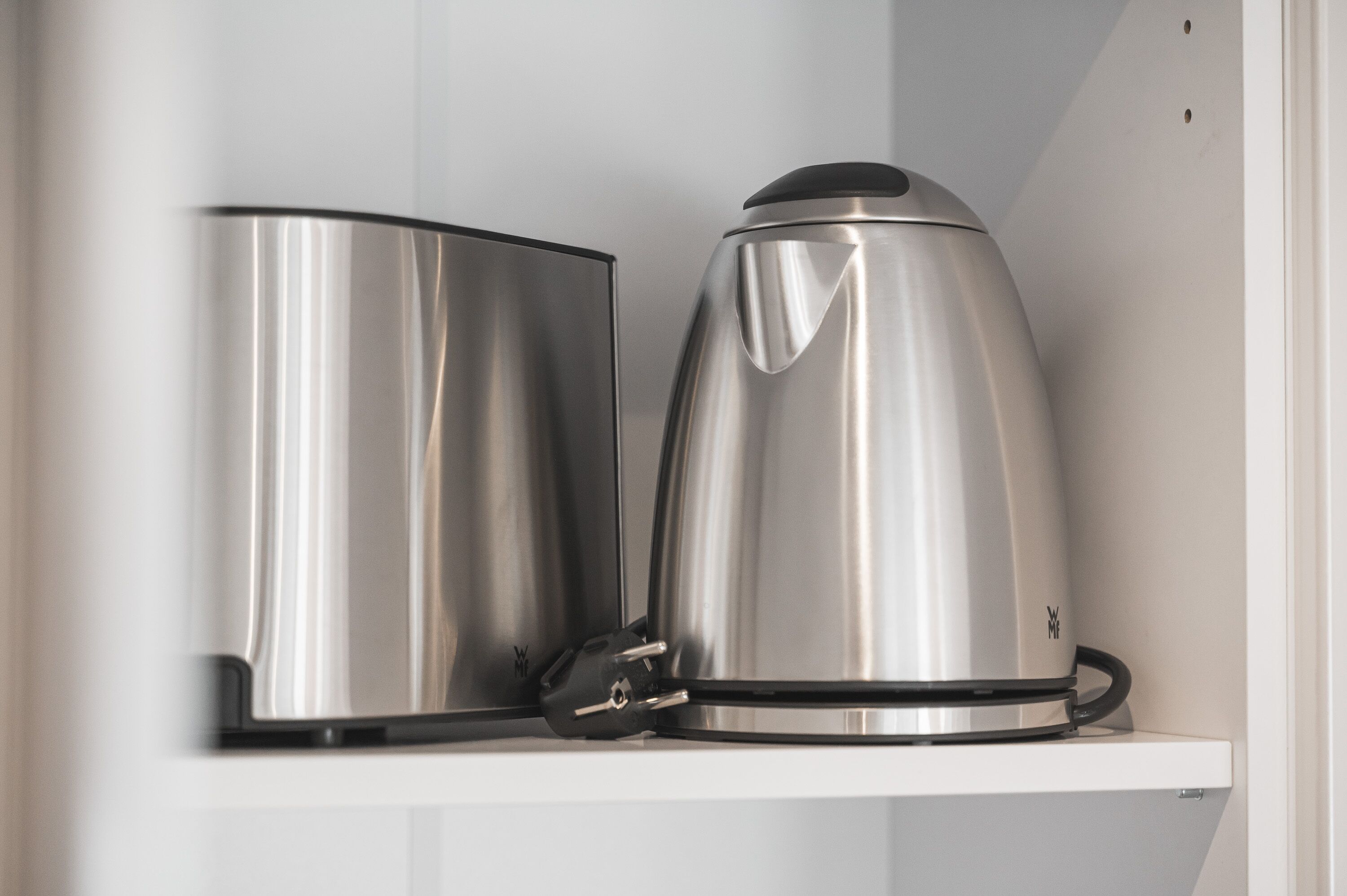 A stainless steel kettle and a coffee pot on a white shelf.
