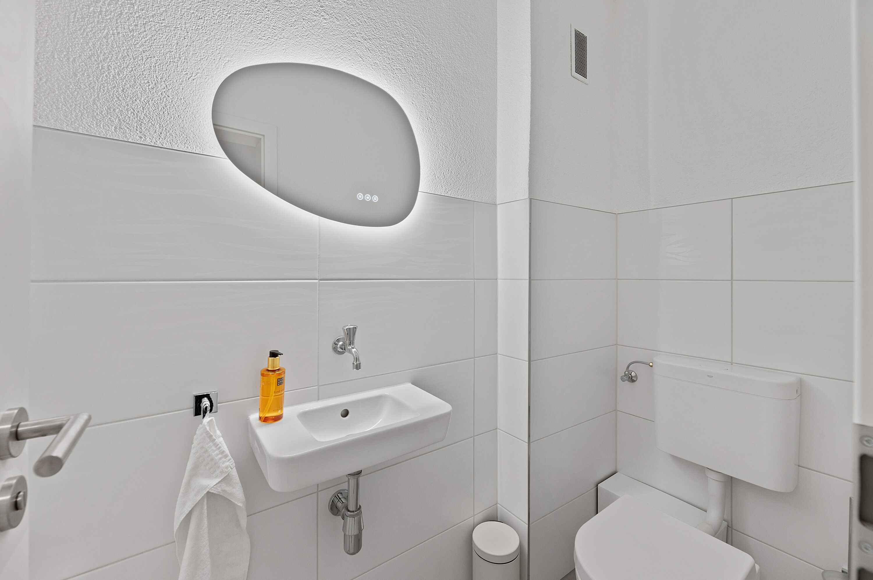 Ein modernes Badezimmer mit einem weißen Waschbecken, einem Spiegel und einer Toilette.