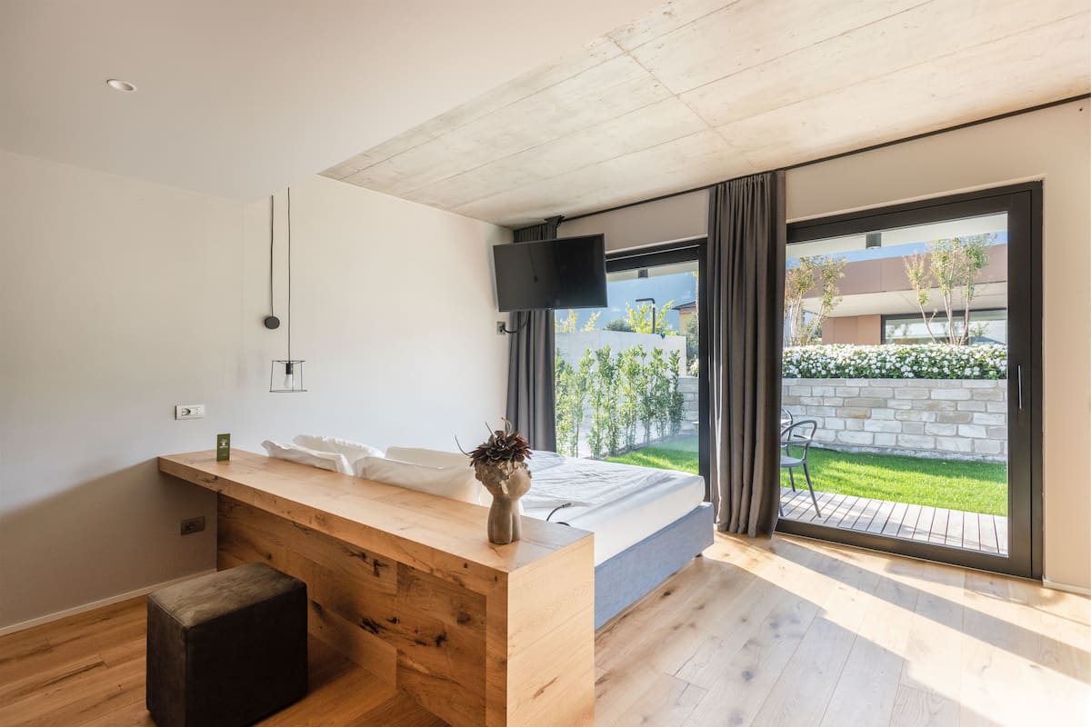 Une chambre moderne avec un bureau en bois, un lit, une télévision et une vue sur un jardin, accessible par une porte coulissante.