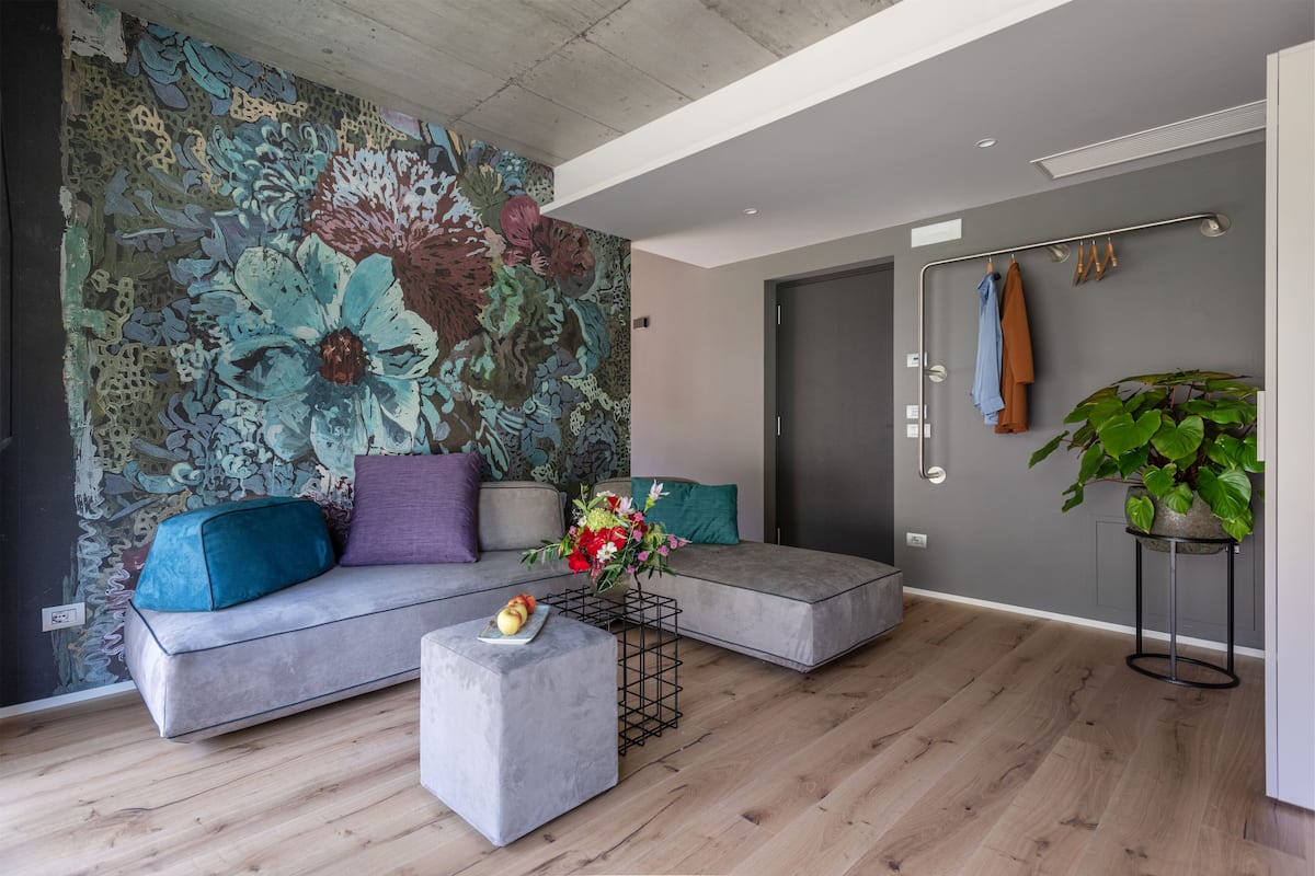 Un salon moderne avec un canapé gris, une petite table basse et une fresque murale aux motifs floraux éclatants.