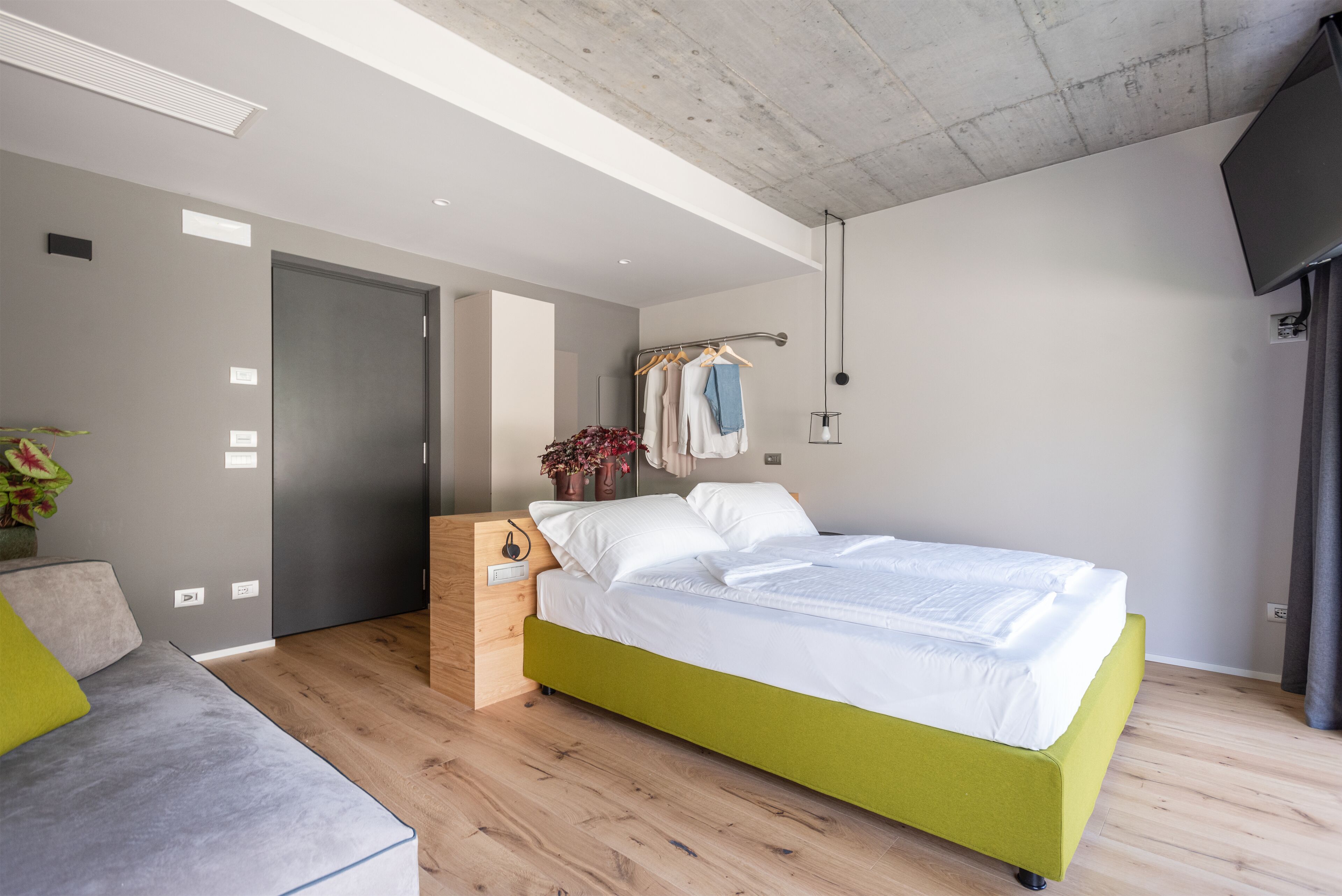 Een moderne slaapkamer met een groen bed, houten vloeren en een grijze bank.