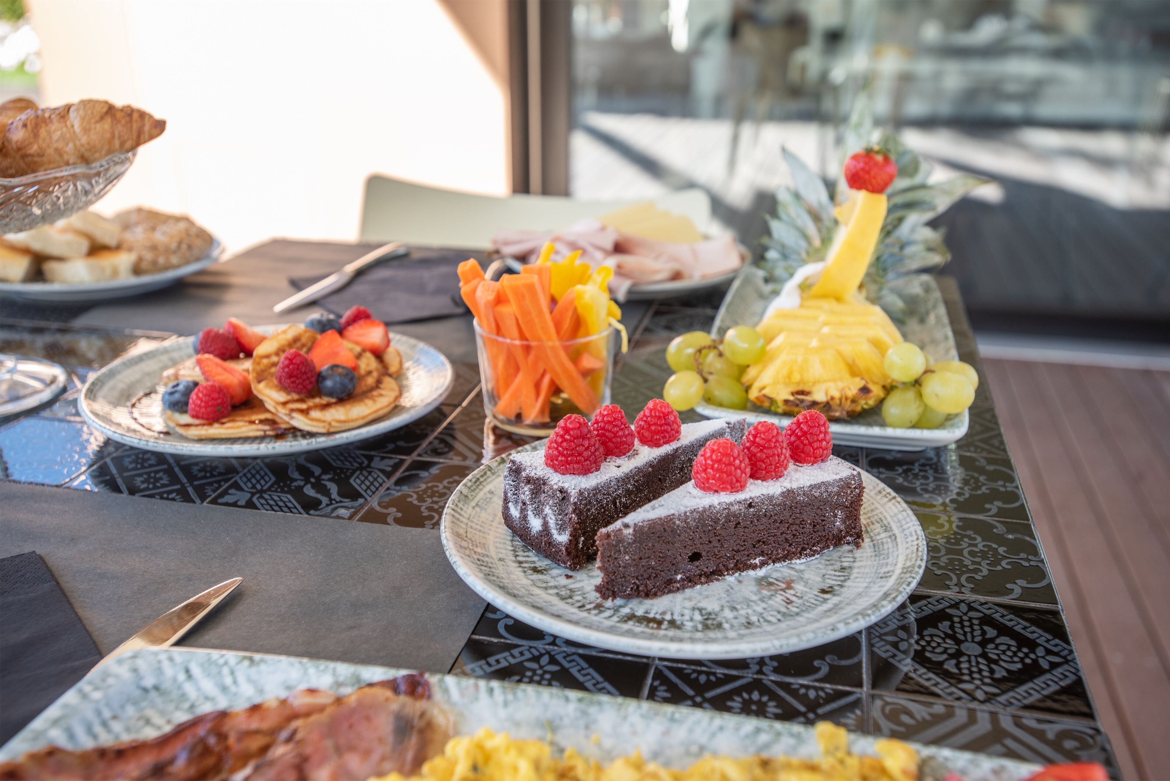 A breakfast buffet with various dishes including pastries, fruits, and a slice of cake.