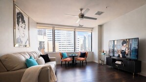 Een moderne woonkamer met een bank, stoelen, een televisie en grote ramen met uitzicht op de stad.