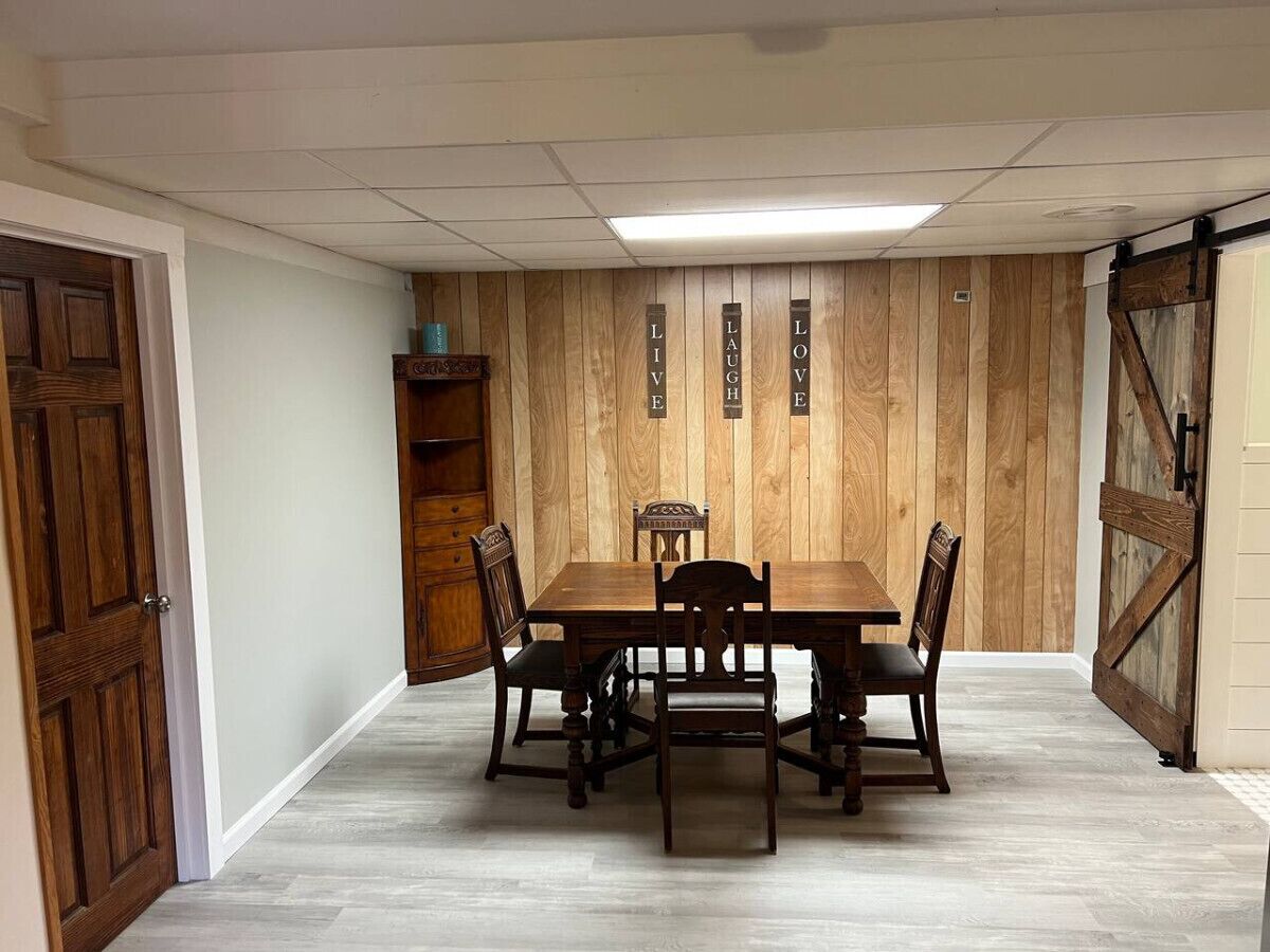 A dining room with a wooden table and chairs, a wooden wall with vertical text, and a door on the left.