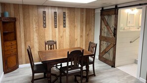 A dining area with a wooden table and chairs, a wooden cabinet, and a sliding barn-style door. - ​​2BR w/ Fireplace | Backyard Seating + Firepit (Wellsboro)
