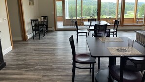 A spacious dining area with multiple tables and chairs, large windows offering a view of the outdoors, and a wooden floor. - Sunny 1BR w/ Game Room + Firepit | 10 min to Town (Wellsboro)