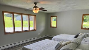 A bedroom with two beds, a ceiling fan, and large windows with a view of a grassy yard. - King Suite Near Town + Trails~Game Room + Firepit (Wellsboro)