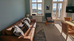 Un salón con un sofá de cuero marrón, una silla de madera, un escritorio y un ventanal con vistas a la ciudad.