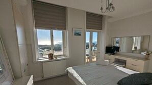 Un dormitorio con cama, cómoda, televisor y una ventana grande con vistas al exterior.