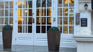 Una entrada de edificio con un gran arco, dos macetas y un letrero que indica accesos a las alas oeste y este.