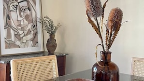 A dining table with a vase of dried flowers, a bowl, and a framed artwork on the wall. - Unique Design | Hot Tub | Brookside | Gathering Pl (Tulsa)